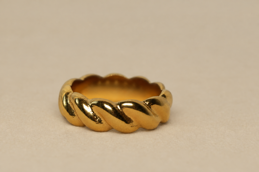 A gold ring with a textured, ridged outer band and a smooth inner band, photographed on a neutral beige background.